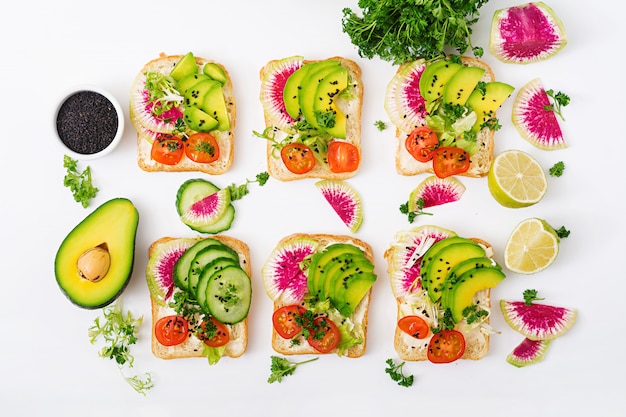 Vegan sandwiches met avocado, watermeloen radijs en tomaten op een witte tafel.