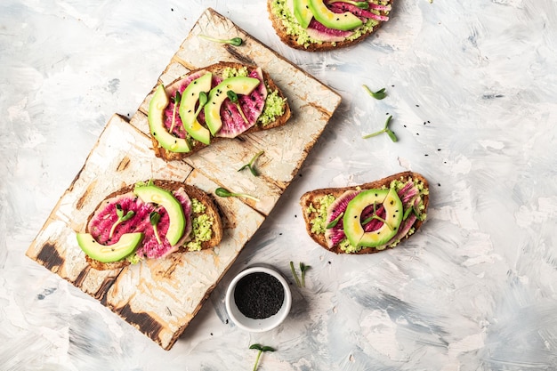 Vegan sandwiches with avocado watermelon radish and microgreen Delicious breakfast or snack on a light background top view