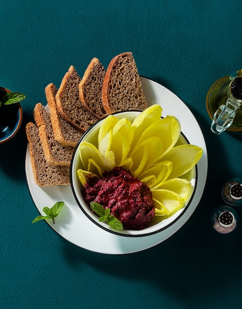 Vegan snack of spread of roasted beets and pistachios and leaves of Belgian Endive with whole grain bread on the table