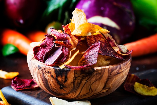 Vegan snacks multicolored vegetable chips in wooden bowl and set of fresh farmer vegetables rustic still life selective focus