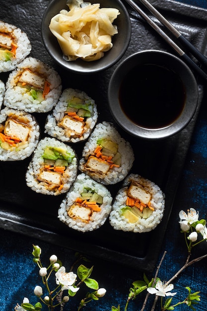 Vegan sushi met tofu in General Tso saus avocado en verse groenten op een tafel met takken van een bloeiende boom