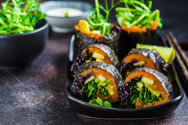 Vegan sushi rolls with black rice, avocado and sweet potato on black dish