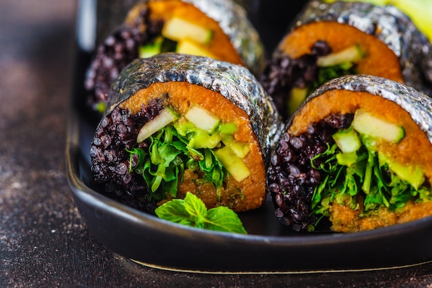 Vegan sushibroodjes met zwarte rijst, avocado en zoete aardappel op zwarte schotel