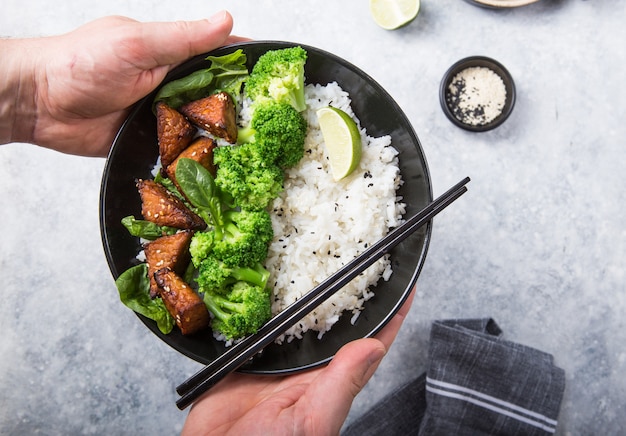 Vegan teryaki tempeh of tempe boeddha kom met rijst, gestoomde broccoli, spinazie en limoen op grijze achtergrond. gezond eten