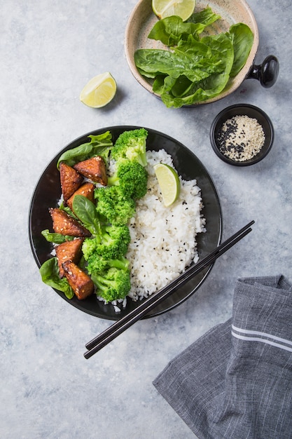 Photo vegan teryaki  tempeh or tempe buddha bowl  with rice, steamed broccoli, spinach  and lime on gray background. healthy food