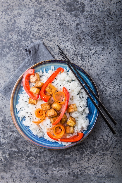 Веганские тофу тыкать миску с рисом, перцем, морковью и тмином в керамической миске, серый фон.