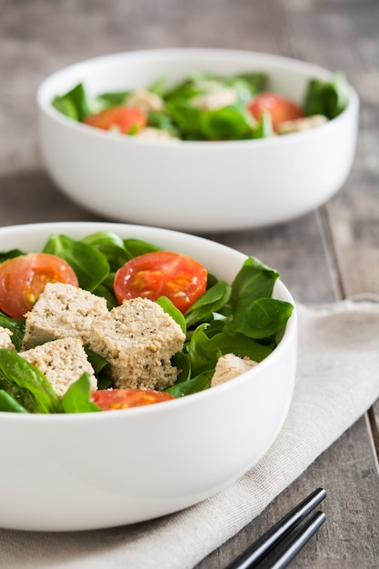 Vegan tofu salad with tomatoes and lamb's lettuce on wooden table