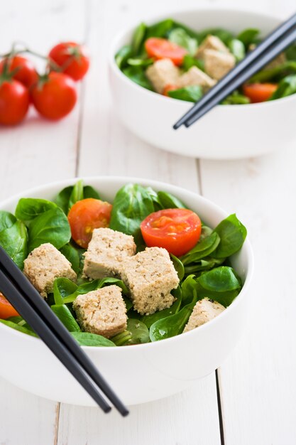 Vegan tofu salade met tomaten en veldsla op witte houten tafel