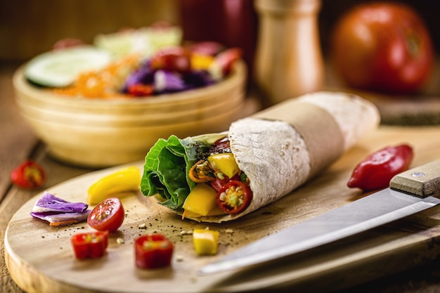 Vegan tortilla wrap, vegetarian roll with grilled vegetables, pepper, lentils, tomatoes and cabbage, on a rustic wooden surface