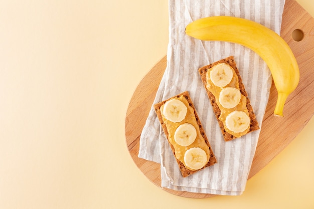 Vegan volkoren knäckebröd met pindakaas en plakjes banaan voor een licht diner op geel