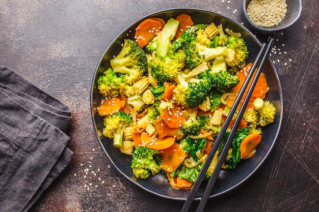 Photo vegan wok stir fry with broccoli and carrot in black dish, top view, copy space.