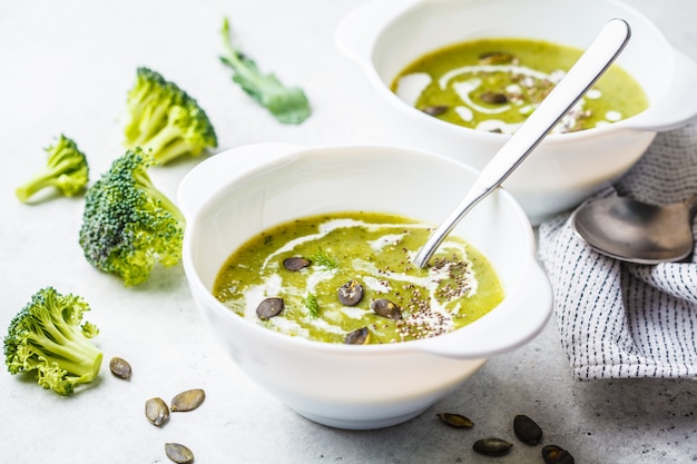 Veganist detox broccoli crème soep met kokos room en pompoenpitten in witte kom, kopie ruimte.