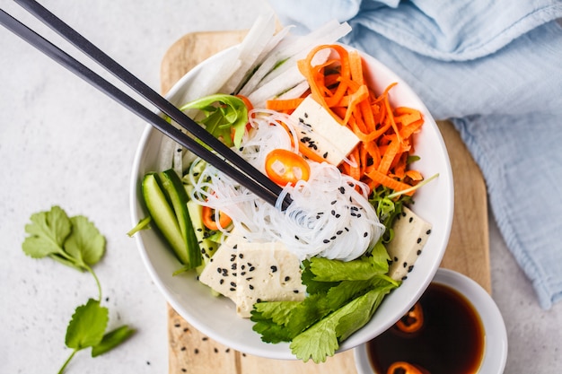 Veganistisch broodje cha saladeschaal. Vietnamese rijstnoedel met tofu en Spaanse pepersgroenten salade in witte kom