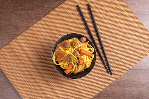 Veganistisch eten Veganistische Yakisoba met eetstokjes in een kom op bamboemat over houten bovenaanzicht