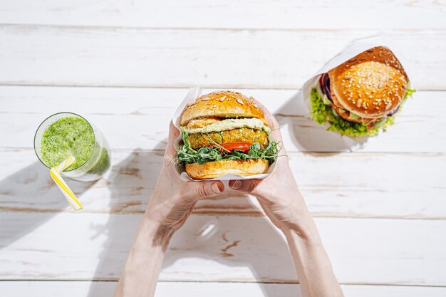 Veganistisch met een klontje glutenvrij met lijnzaad kikkererwtenburgers met rucola, radijs, avocado, komkommer en hummus Plantaardig dieetconcept Burger in de handen van een vrouw die in een openluchtcafé zit
