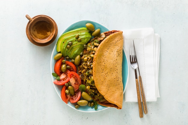 Veganistisch ontbijt van glutenvrije ei-vrije kikkererwtenomelet met gebakken champignons en prei. en een salade van verse rijpe tomaten, avocado's, olijven en kappertjes.