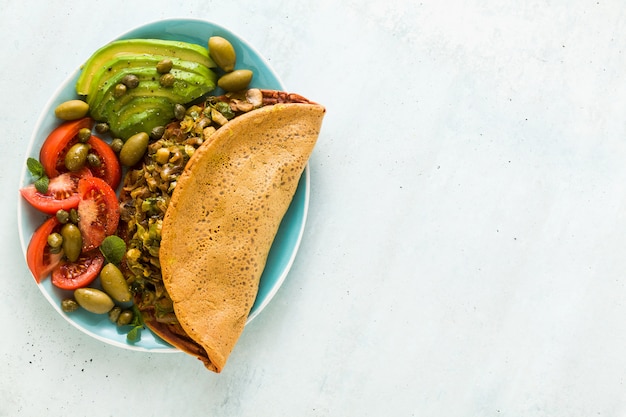 Veganistisch ontbijt van glutenvrije ei-vrije kikkererwtenomelet met gebakken champignons en prei. en een salade van verse rijpe tomaten, avocado's, olijven en kappertjes.