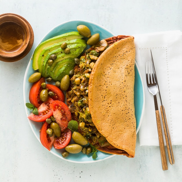 Veganistisch ontbijt van glutenvrije ei-vrije kikkererwtenomelet met gebakken champignons en prei. en een salade van verse rijpe tomaten, avocado's, olijven en kappertjes.