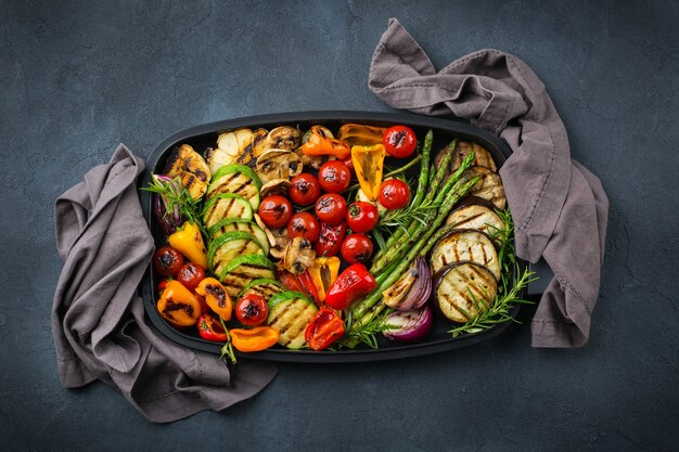 Veganistisch, vegetarisch, seizoensgebonden, zomers eetconcept. gegrilde groenten in een pan op een donkere zwarte tafel. bovenaanzicht plat lag achtergrond