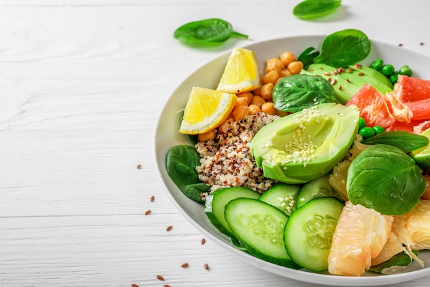 Veganistisch voedselconcept: quinoa met avocado, komkommers, groene erwten, kikkererwten, spinazie en citrusvruchten op witte backround.