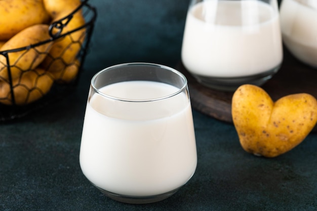 Veganistische aardappelmelk in glas en aardappel in kom op donkere achtergrond Veganistische melk Plantaardige melkvervanger en lactosevrij Plantaardige melk