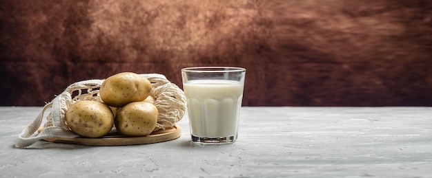 Veganistische aardappelmelk in glas en rauwe aardappel alternatieve plantaardige melk gezonde voedingstrend gezond schoon eten veganistisch of glutenvrij dieet lang bannerformaat bovenaanzicht