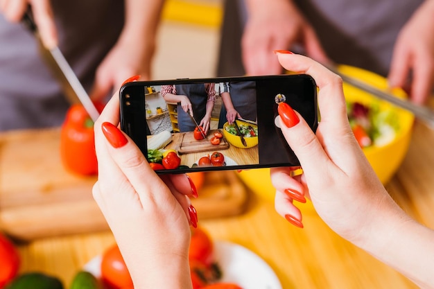 Veganistische culinaire videoblog Close-up van vrouwelijke handen die smartphone vasthouden om vrouwen te filmen die groentesalade bereiden