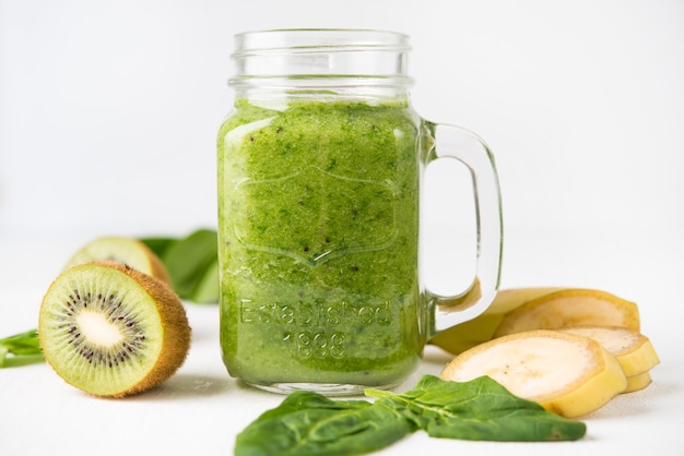 Veganistische groene smoothie in een pot met spinazie, banaan en kiwi op een witte ondergrond