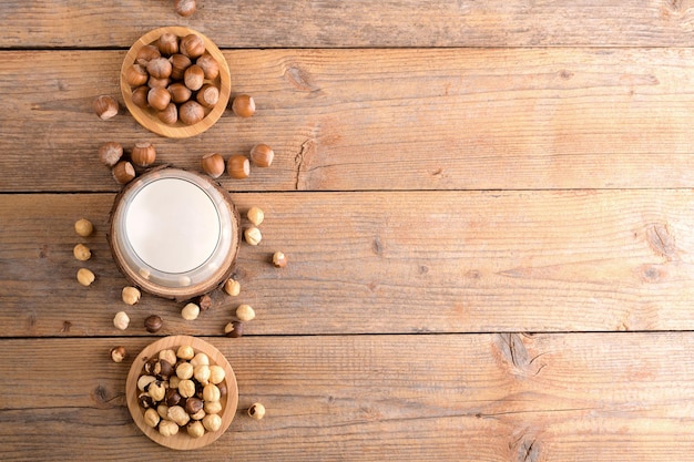 Veganistische hazelnootmelk zonder dagboek in glas met hele hazelnoten op een linnen servet op een rustieke houten achtergrond Lactosevrije hazelnootdrank is plantaardige alternatieve melk Gezond melkproduct bovenaanzicht