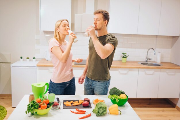 Veganistische jonge liefdevolle familie drinkt natuurlijke smoothie tijdens het koken van rauwe groenten in de keuken.