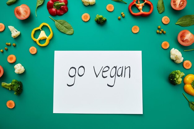 Foto veganistische levensstijl ga veganistisch belettering geschreven op papier geplaatst tussen verse groenten op groene achtergrond