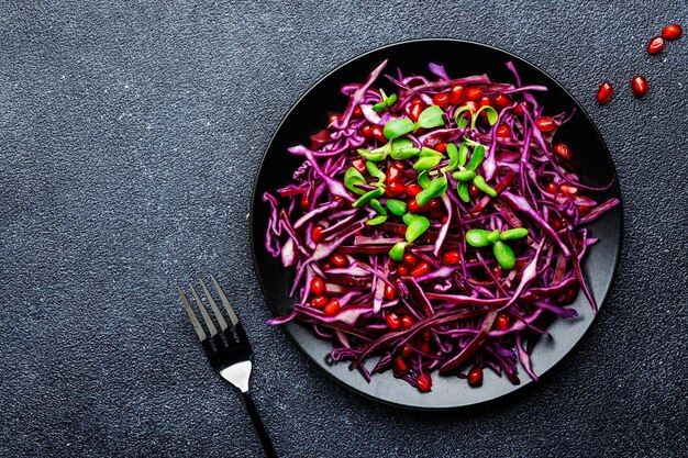 Veganistische salade met rode kool peterselie granaatappel zaden zonnebloem spruiten en olijfolie dressing op zwarte keukentafel achtergrond bovenaanzicht