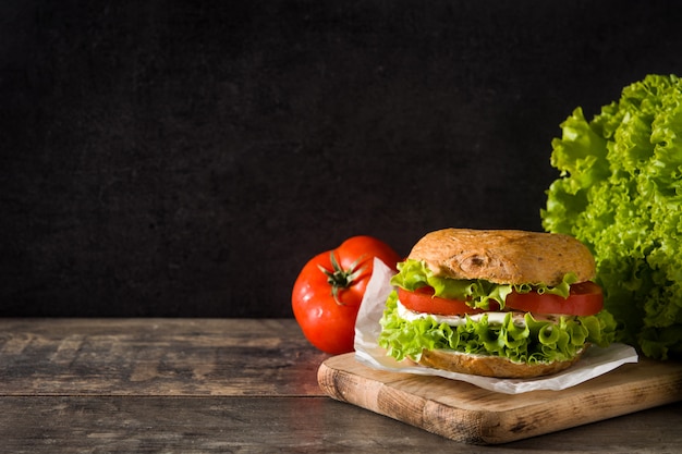 Vegetable bagel sandwich with tomato, lettuce, and mozzarella cheese on wooden table Copy space