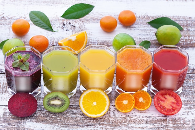 Photo vegetable and citrus juices pieces of vegetables and fruits on wooden desk unusual top view