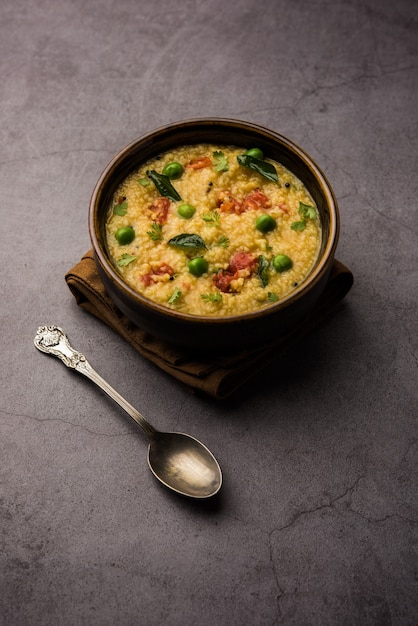 Vegetable Dalia or Daliya Khichadi or Broken Wheat Khichdi with tomato, green peas and chilli, served in a bowl or plate