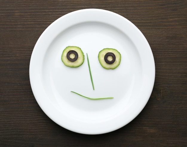 Photo vegetable face on plate on wooden table