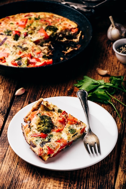 Vegetable frittata with broccoli, red bell pepper and red onion\
on white plate and in a cast iron