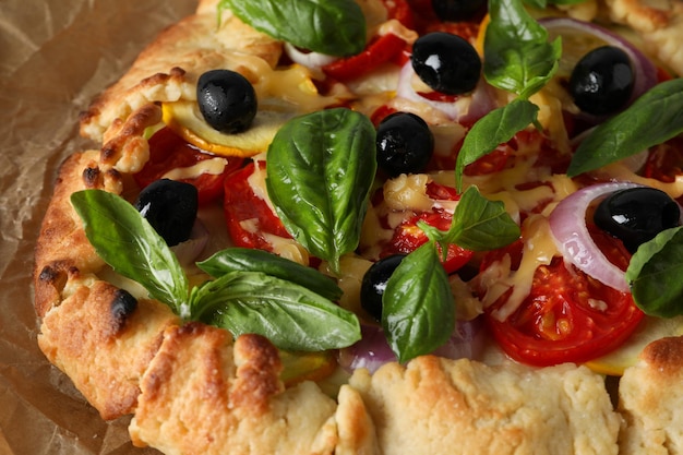 Vegetable galette with olives and basil on parchment paper close up