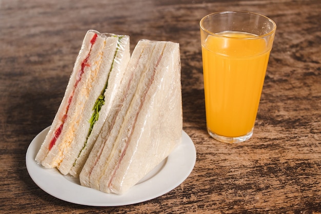 Vegetable and ham and cheese sandwiches, with orange juice on a wooden table.