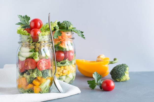 Vegetable healthy homemade colorful salad in mason jar with tomato lettuce broccoli on blue Copy space Lunch for work Food set