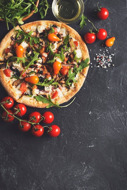 Foto pizza italiana di verdure con pomodori su sfondo nero, copia spazio, vista dall'alto, verticale