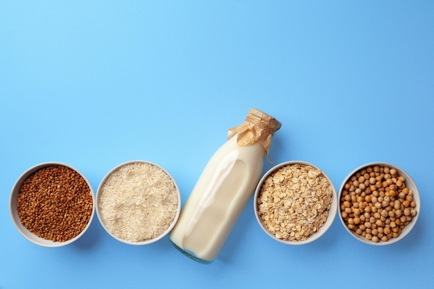 Vegetable milk concept with milk bottle and bowls with grains and nuts on blue background top view