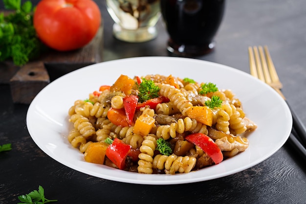 Vegetable pasta fusilli corti bucati with eggplant sweet pepper and chicken in white plate on dark table