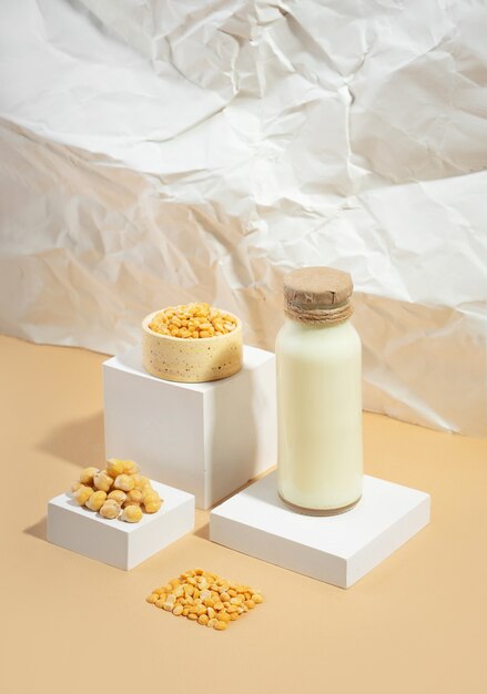 Vegetable pea milk in a bottle and chickpeas in bowl on white podium,pedestal on beige crumpled paper background. shadows. lactose free vegan product.Modern composition.Isometric diagonal projection