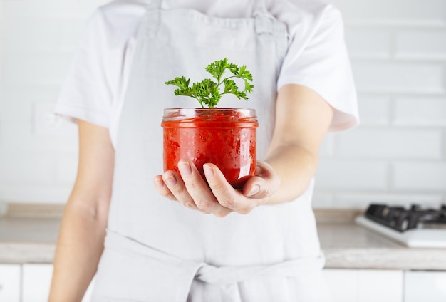 Vegetable salad ajvar in the hands of a woman in a jar sweet peppers eggplant tomatoes spices