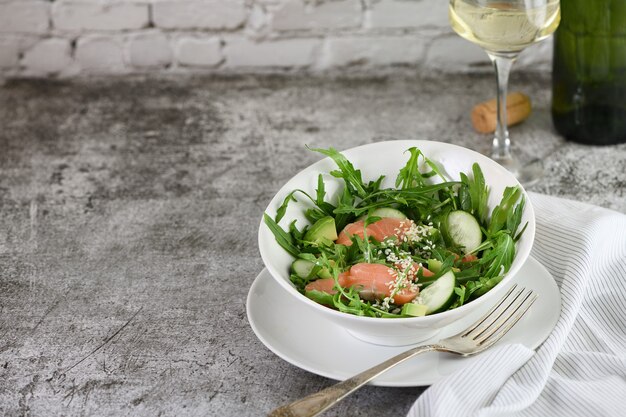 Vegetable salad from arugula, avocado and cucumber pieces with the addition of tender salted salmon, seasoned sesame seeds