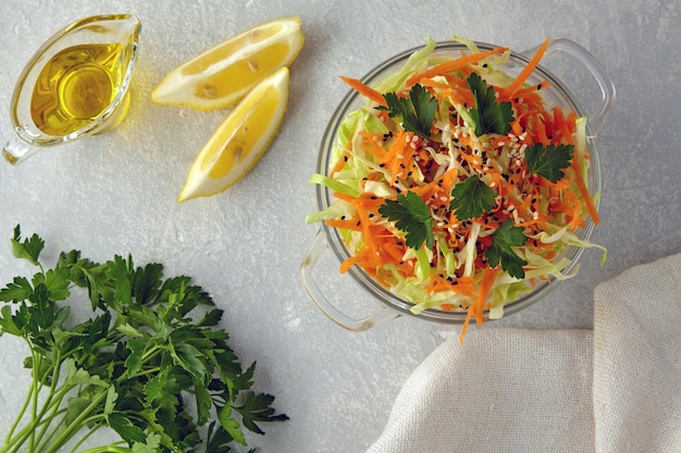 Vegetable salad of grated cabbage and carrots with lemon and olive oil dressing garnished with parsley on a gray concrete table Top view with copy space