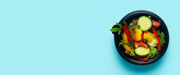 Vegetable salad in a plastic disposable bowl on a light blue background. Top view, flat lay. Banner.