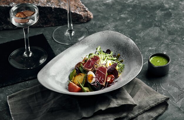 Insalata di verdure con tonno fresco e avocado di agrumi in un piatto grigio su un'ardesia grigia