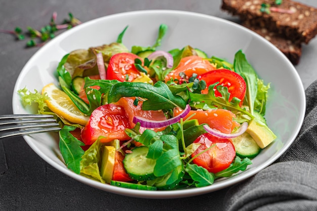 Овощной салат с лососем и свежей зеленью на темном фоне